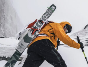 Jim Morrison with skis on his back climbing up a steep snow slope.