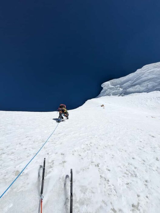 A climber on an ice ramp, roped up to the photographer who has left his two ice-axes on the ice to shoot the picture. 
