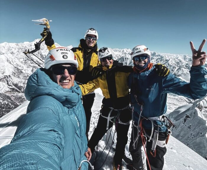 Four climbers smile on a snowy summit.