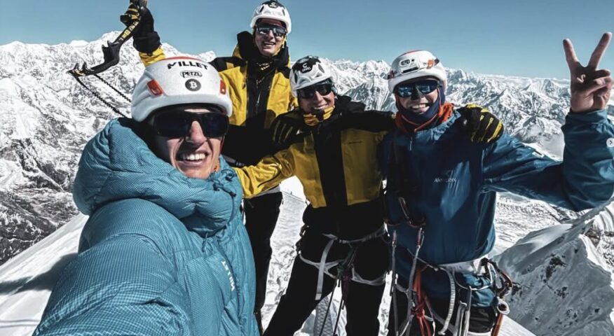 Four climbers smile on a snowy summit.