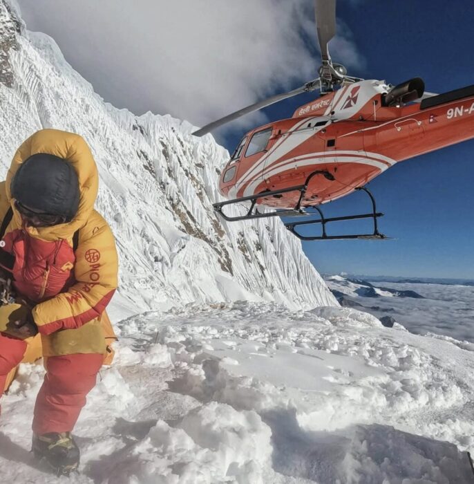 A climber looks down to avoid the snowdust raised by a helicopter at high altitude on Manaslu. 