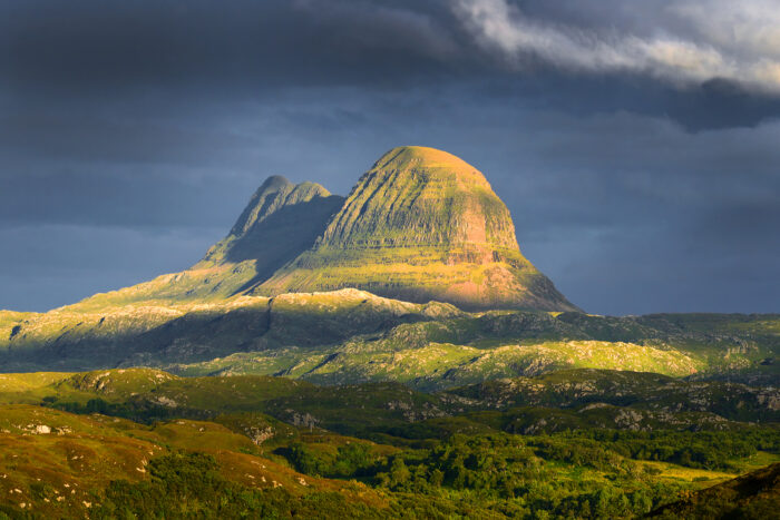 A sunlit peak (Suilven) emerges from the rocky lowlands