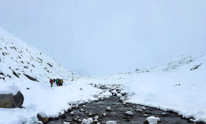 trekkers in a fogy day on snowy paths by a river.