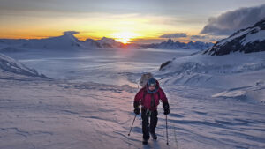 A climber on a huge, flat ice plain with mountains in background at sunset.