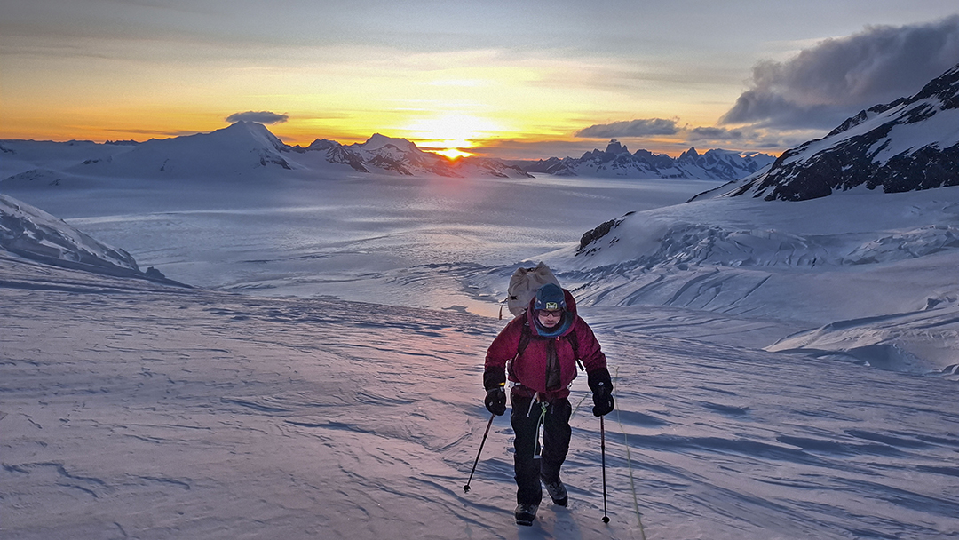 A climber on a huge, flat ice plain with mountains in background at sunset.