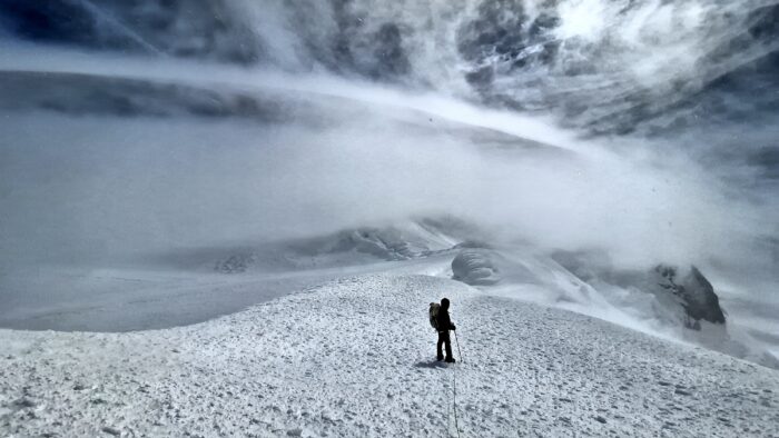 A climber among clouds on a wide snowy summit.