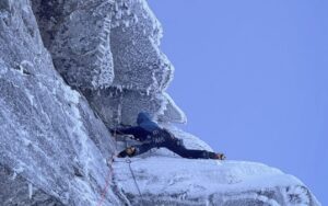 A climber on crampons and iceaxes on a frosted granite face in Scotland.