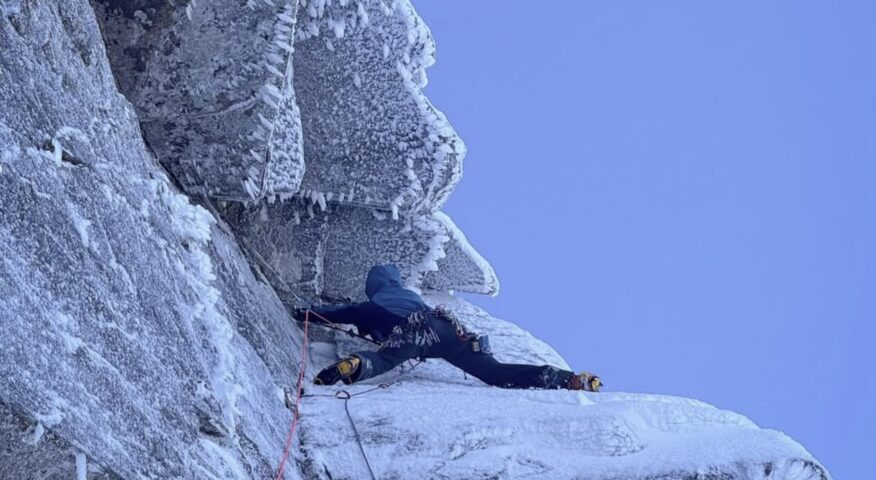 A climber on crampons and iceaxes on a frosted granite face in Scotland.