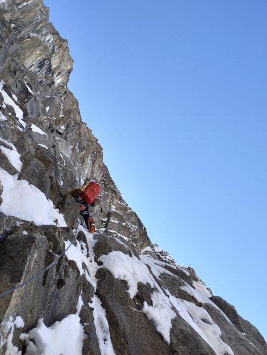 A climber on rocky ledges spotted with snow.