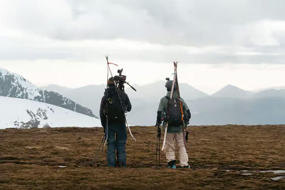two skiers standing on moss looking at snowy peaks