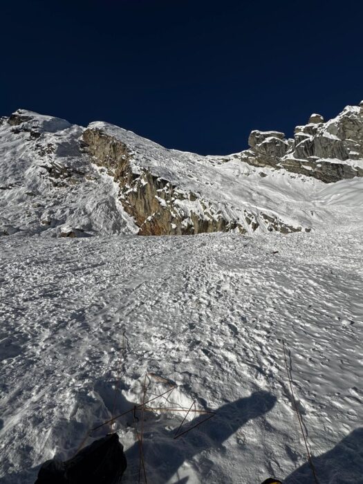 A wide field of avalanche debris on mild terrain under a peak's cliff. 