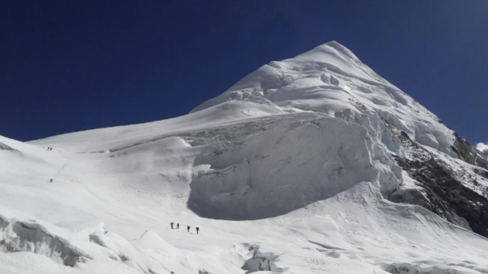 Climbers on a snowy peak, walking to the left to avoid a gib serac barrier towards a col.