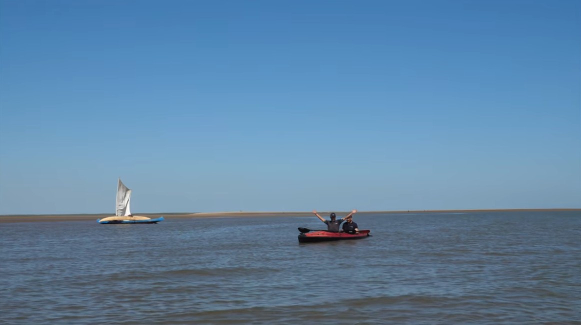 Two men in a kayak on a broad blue channel