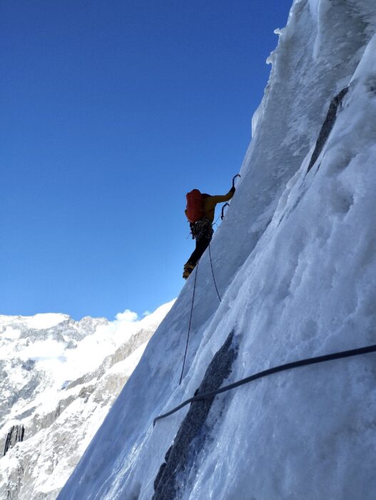 A climber in a smooth ice wall in the shade.