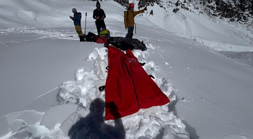 Four rescuers on a snowy surface where they have dug avalanche victims and covered them with a red blanket.