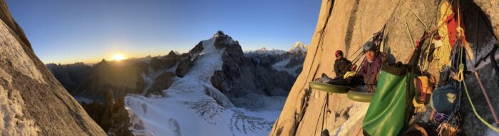 Climbers on an inflatable portaledge on a granite spire at dawn.