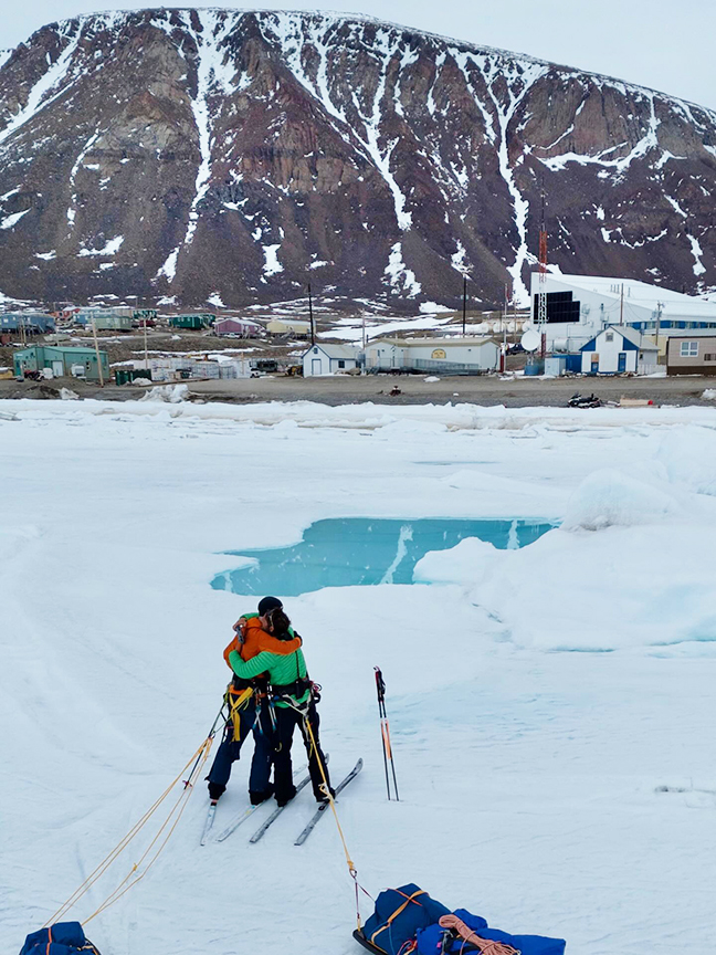 two skiers embrace in front of an arctic village