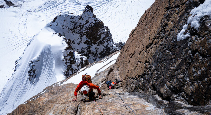 Two climbers ona granite wall, snowy glaciers at their feet.