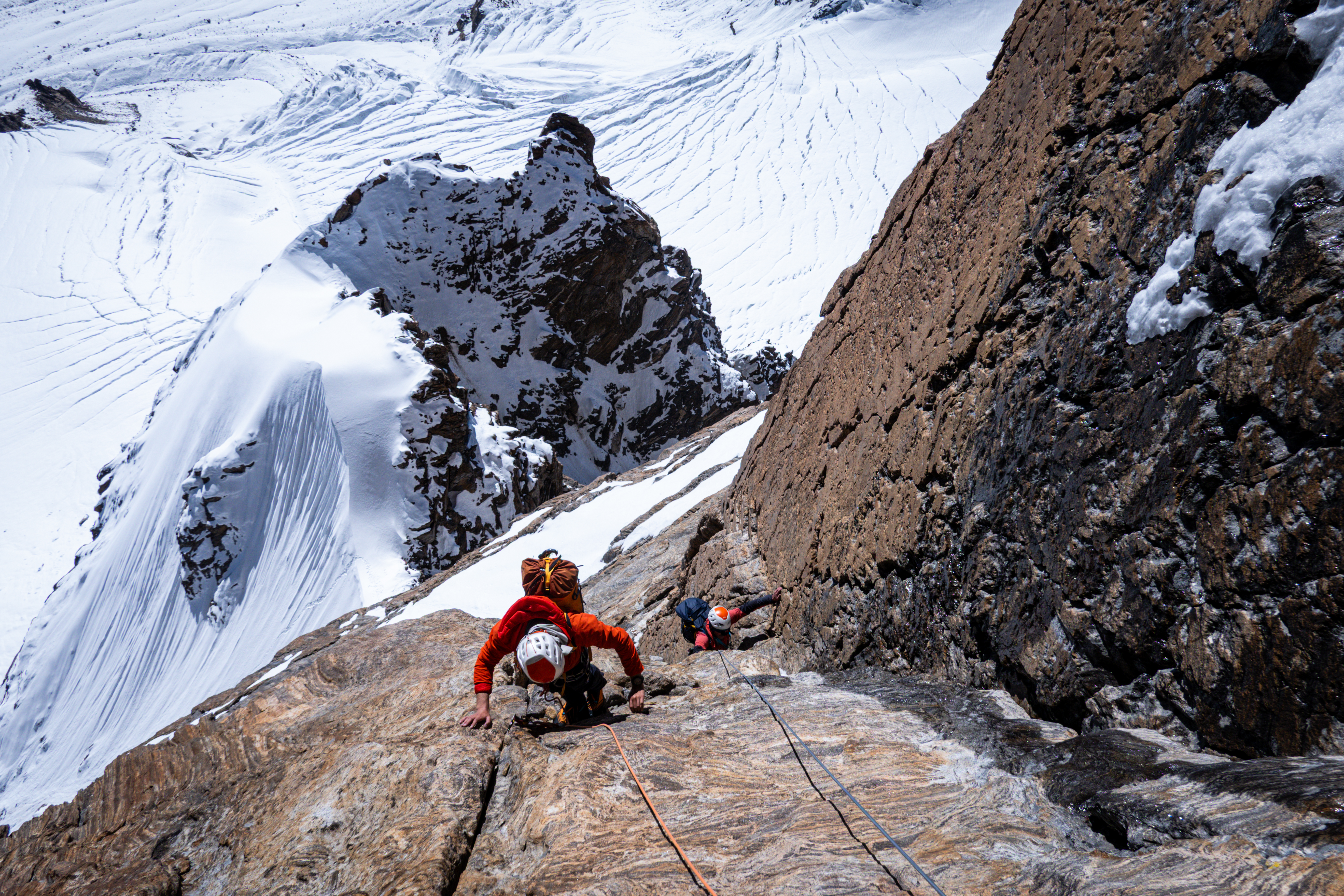 Two climbers ona granite wall, snowy glaciers at their feet.