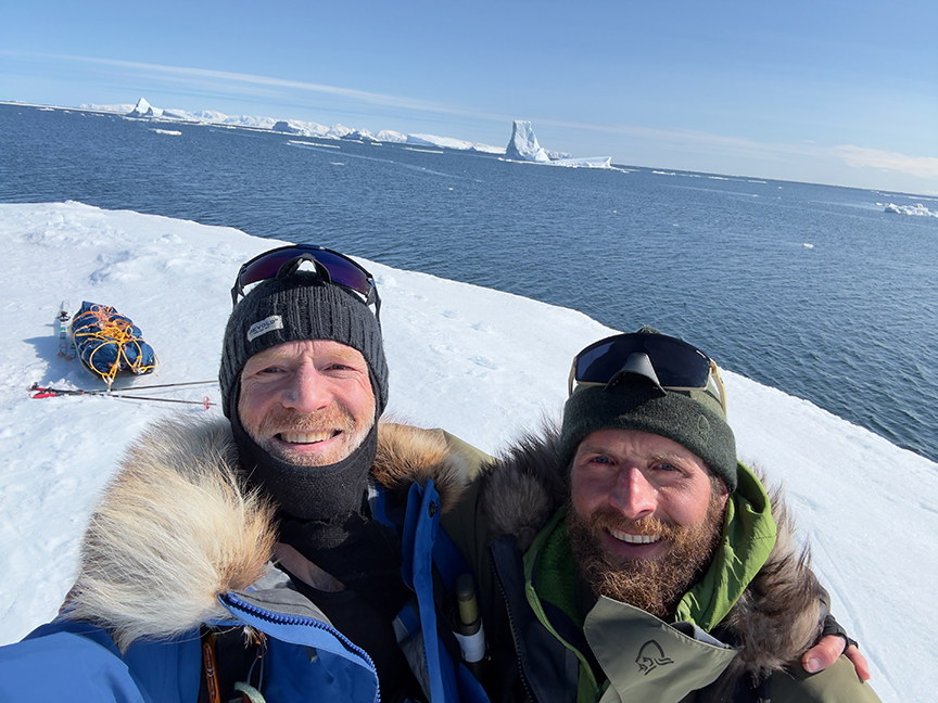 two polar travelers standing beside open water