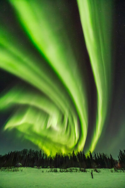 A green aurora lights up the sky in an aerial spiral