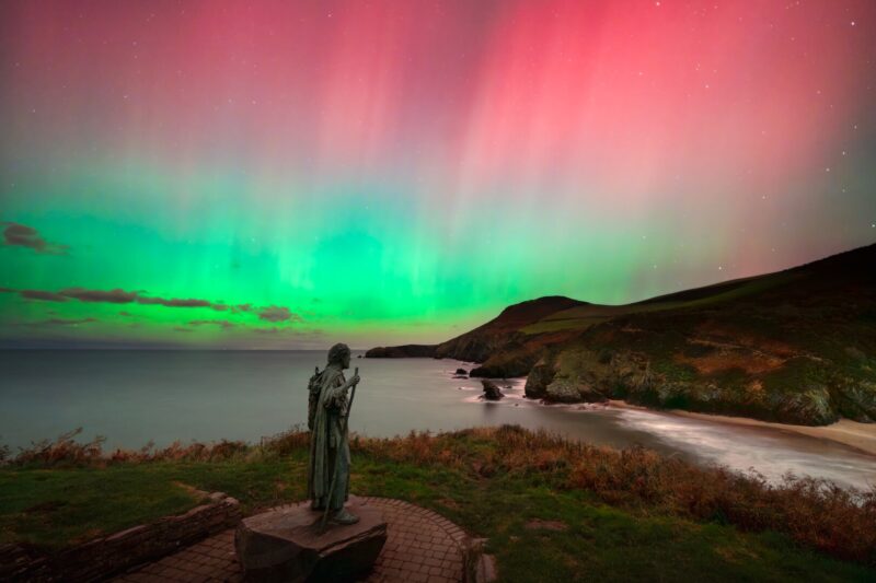 Northern Lights display on the rugged Ceredigion coast of West Wales over a statue of St. Crannog