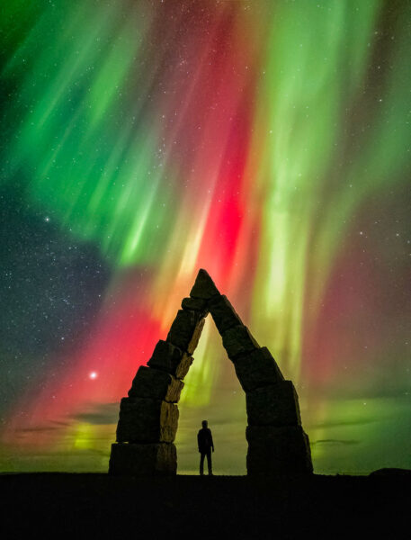 Silhouette of a man standing in a stone archway against a backdrop of the Northern Lights