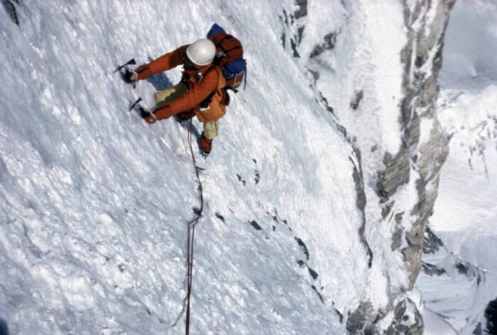 A climber in 1980's gear on a vertical ice and rock face.