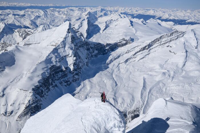 Two climbers with skis on their backpacks on the summit of Mt. Robson, surrounded by snowy peaks int he Canadian Rockies.