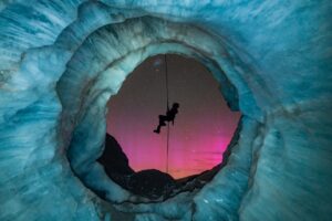The silhouette of a climber in the mouth of an ice cave against the aurora