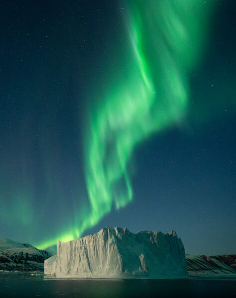 A bright green aurora twists over an iceberg