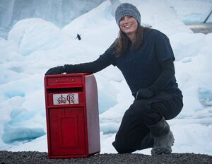 A woman smiling beside a small red postbox