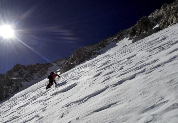 A climber on a wind-swept snow ramp. 