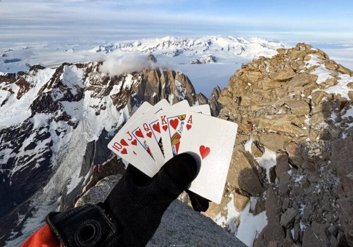 A clibmer's globed hand shows poker cards on a Patagonian summit.