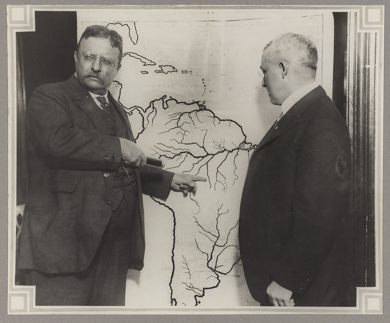 Two men standing in front of a map of South America
