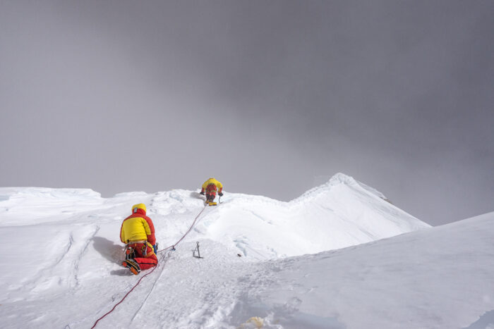 Climbers hunching in high winds on a ridge. 
