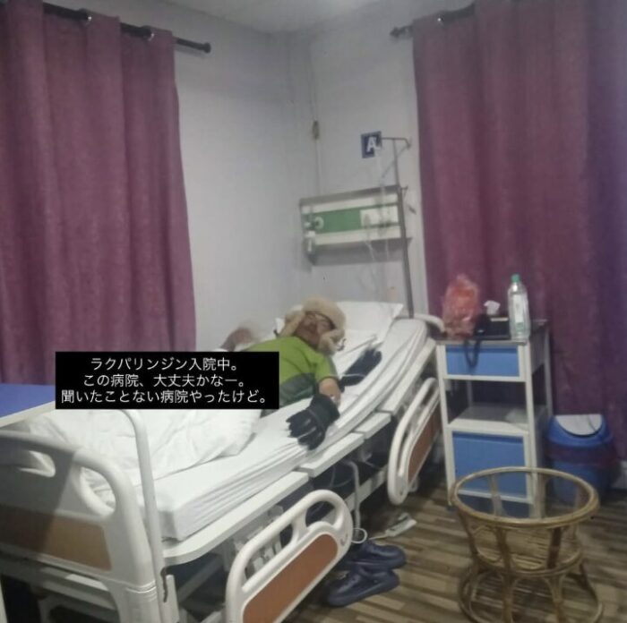 A sherpa in a hospital bed with hand in a special globe and a furry hat on. 