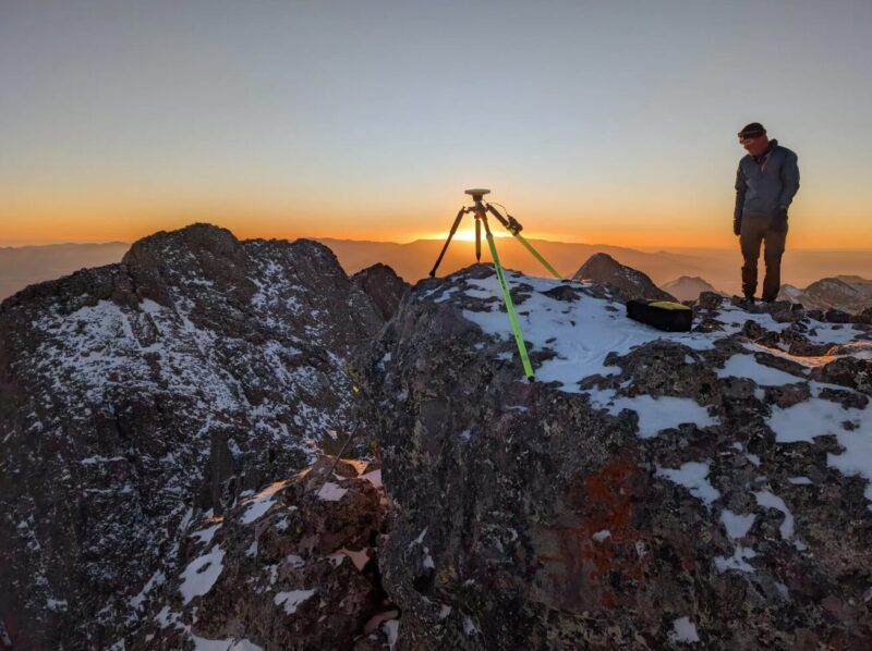 A climber measuring the hight of Crestone Peak in Colorado, with East Crestone in the background