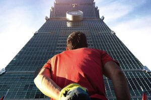 Alex Honnold at Taipei 101 with chalk bag gazing up.