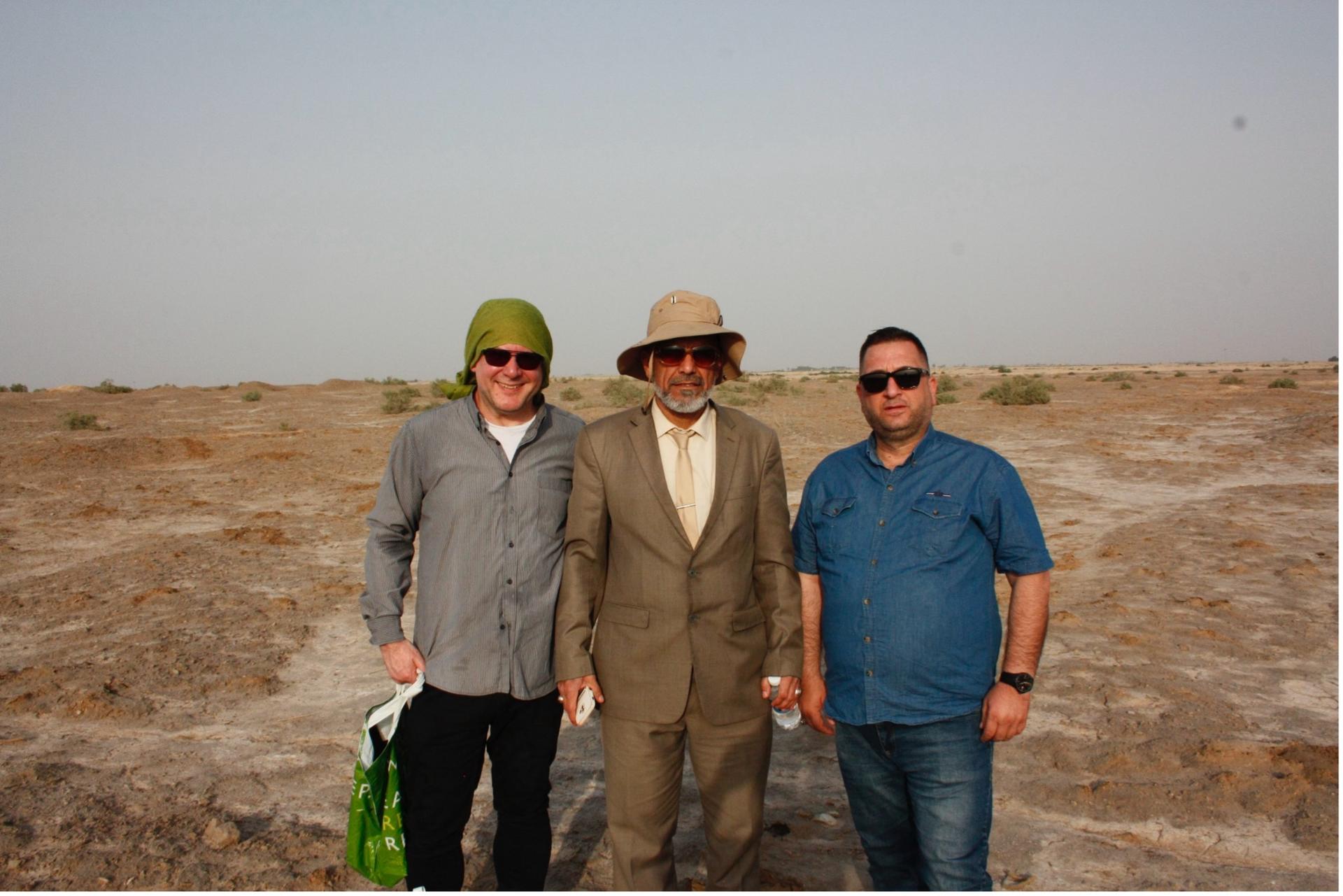 Three men pose at a dig site.
