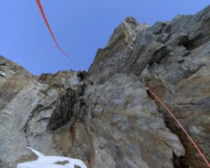 Climbers on an alpine rock face in winter conditions with ropes hanging in the air.