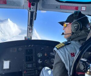 Simone Moro in the cockpit of a helicopter, a snowy peak seen on the windshield.