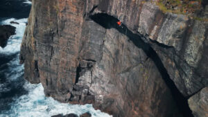 A man climbing a large cliff over the sea