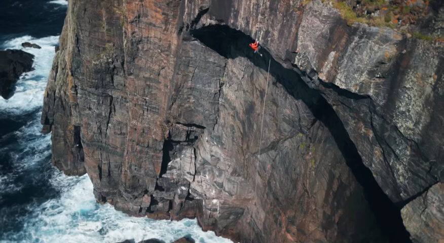 A man climbing a large cliff over the sea