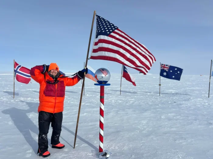 Monet Izabeth standing at the ceremonial South Pole marker in Antarctica.