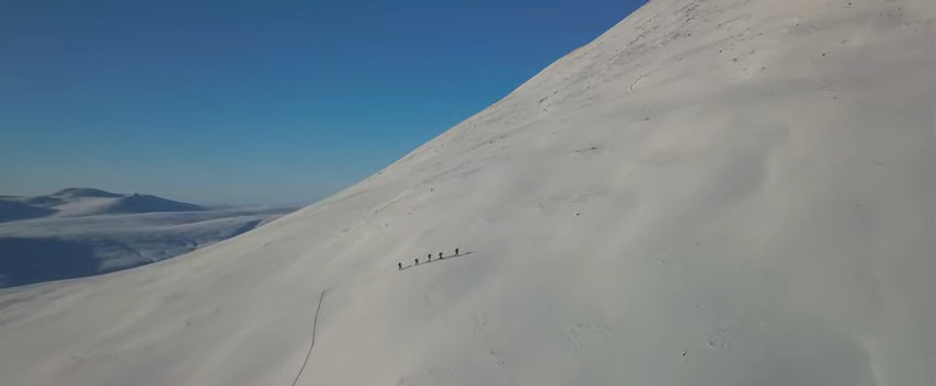 Five small figures walking up a snowy slope