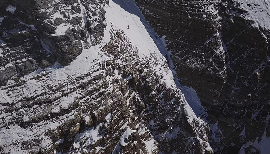 tiny skier on giant dark cliff