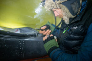 man repairing gear in cold tent