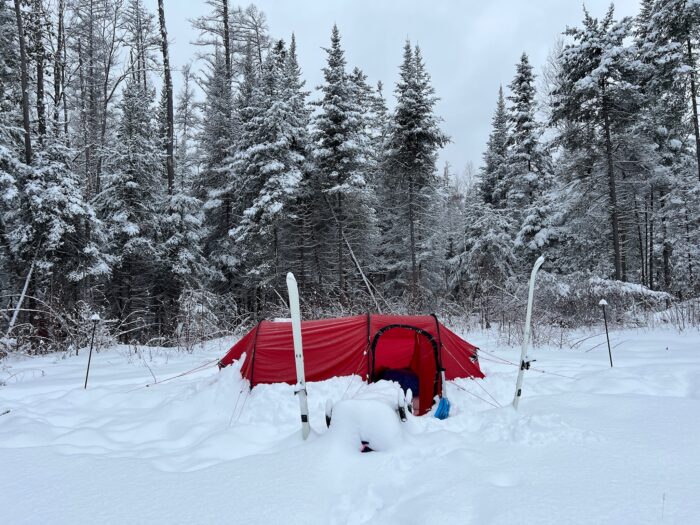 Kneip's red tent pitched in snow surrounded by woodland