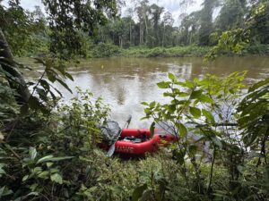 A packraft sits next to the banks of a river in the rainforest of French Guiana